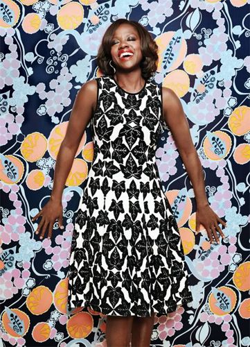 image of actress Viola Davis, a middle-aged black woman, in a leaf-print dress, leaning against a brightly colored wall with her head back and eyes closed, laughing