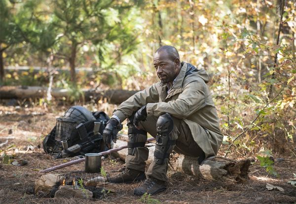 image of Morgan, a middle-aged black man, sitting on a log in a woodland campsite, looking pretty miserable