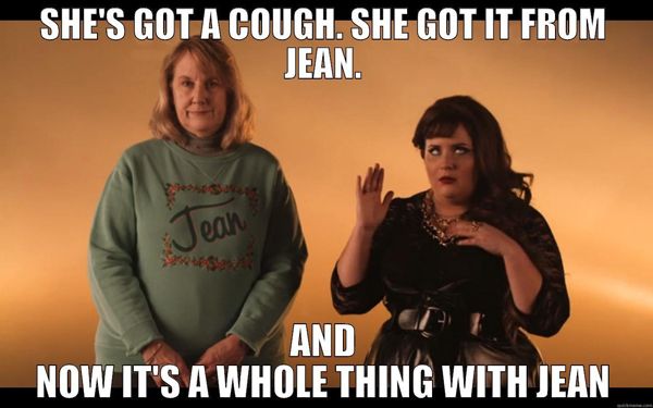 screen cap from video of Aidy Bryant in character, standing next to an older white woman wearing an embroidered sweatshirt reading 'Jean,' to which has been added text reading: 'She's got a cough. She got it from Jean. And now it's a whole thing with Jean.'