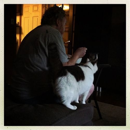 image of Olivia standing beside Iain, who's sitting at the end of the chaise, eating his breakfast