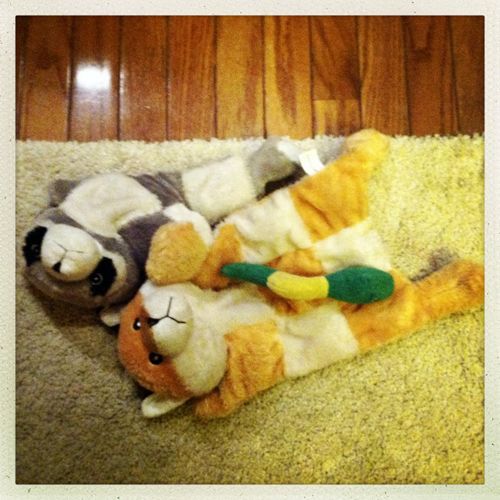 a plush fox lying beside a plush raccoon, with a plush snake lying across the fox's belly