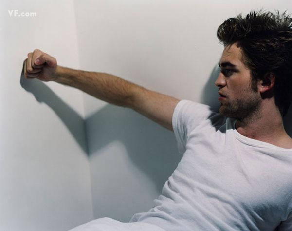 image of Robert Pattinson sitting in a corner looking moody with his fist against a white wall, casting a shadow