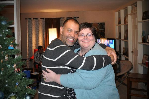 image of Anthony, a trim Latino man in a grey-and-white striped sweater, and me, a fat white woman in a blue sweater and black-and-white patterned blouse, hugging each other tightly and grinning