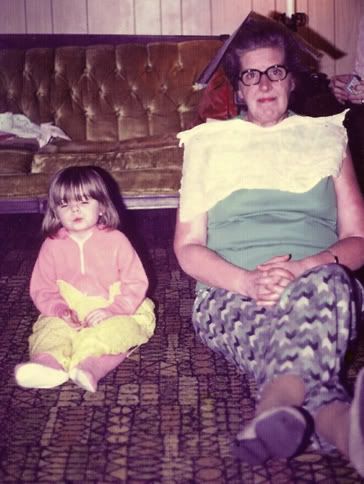 image of me as a toddler, wearing pink footy pajamas and making a silly face, sitting on the floor next to by grandmother, who is wearing a book on her head