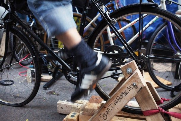 image of feet peddling a stationary bicycle, sitting in a wooden frame which has scrawled on it 'beast of fairness'