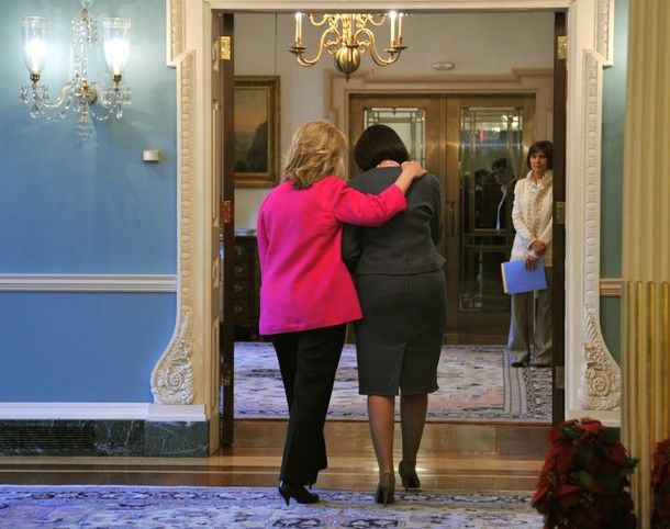 image of Secretary of State Hillary Clinton walking out of a room with Kosovo President Atifete Jahjaga; Clinton's arm is around Jahjaga's shoulders.