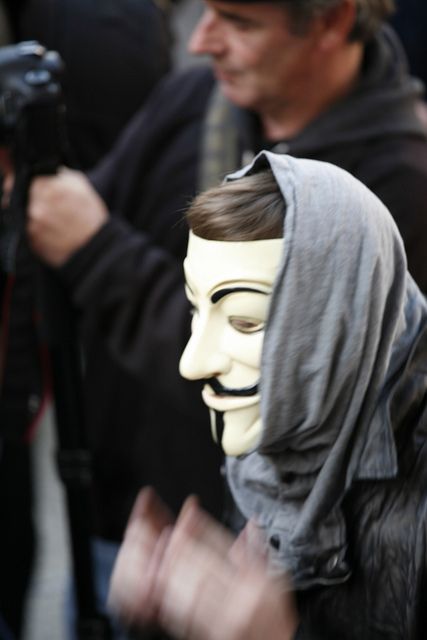 a protestor in a Guy Fawkes mask cheers