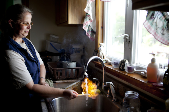 image of a woman standing at her kitchen sink, lighting her tap water on fire
