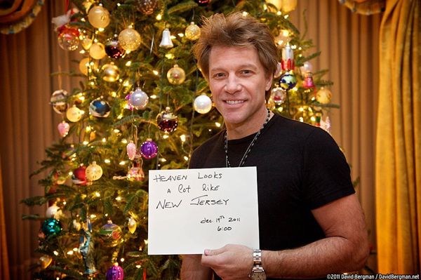 image of Jon Bon Jovi standing in front of a Christmas tree holding a handwritten sign reading 'Heaven looks a lot like New Jersey. Dec. 19, 2011 6:00.'