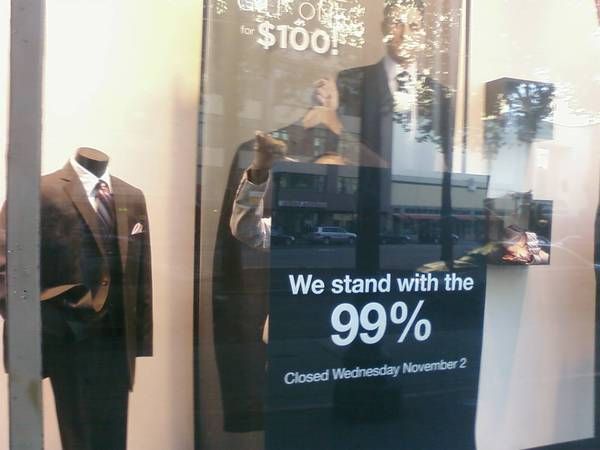 image of an Oakland Men's Wearhouse shop window with a sign reading 'We stand with the 99%. Closed Wednesday November 2.'
