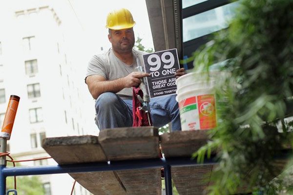 A white male construction worker holds up a sign reading 99 to 1: Those Are Great Odds.