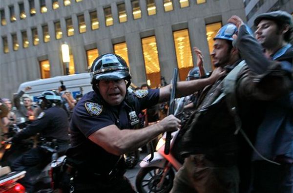 image of police officer shouting at photographer while shoving demonstrator