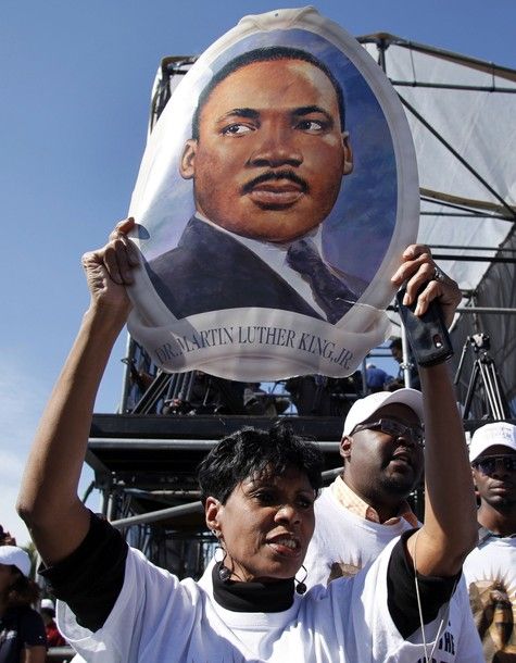 a Black woman holds a portrait of Martin Luther King, Jr. over her head at the dedication of his memorial this weekend in DC