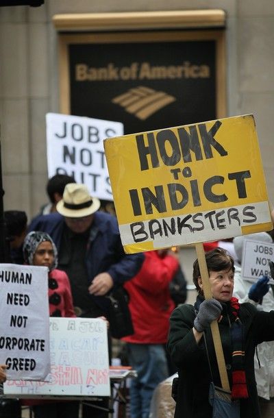 people demonstrate outside the Bank of America in Chicago, holding signs reading: 'Jobs Not Cuts,' 'Jobs Not Wars,' 'Human Need Not Corporate Greed,' and 'Honk to Indict Banksters'