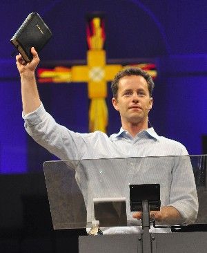 image of Kirk Cameron at a podium holding up a Bible in front of a stained glass window that looks like fiery cross
