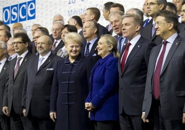 Secretary of State Hillary Clinton and Lithuanian President Dalia Grybauskaite stand in the center of a sea of men; Grybauskaite is looking at Clinton and grinning widely