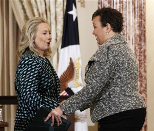 Secretary of State Hillary Clinton, wearing dark trousers and a patterned jacket, and Environmental Protection Agency Administrator Lisa Jackson, wearing dark trousers and a patterned jacket, greet each other with what looks to be 'TWINSIES!' expressions.