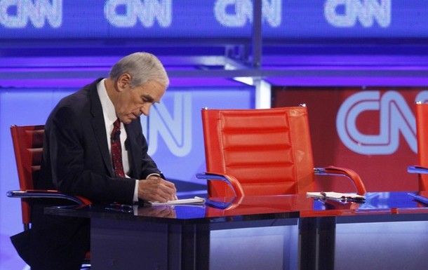 Ron Paul sitting by himself, writing something on a piece of paper