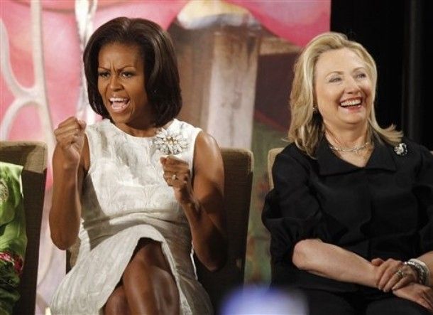 Michelle Obama and Hillary Clinton sit beside one another, grinning