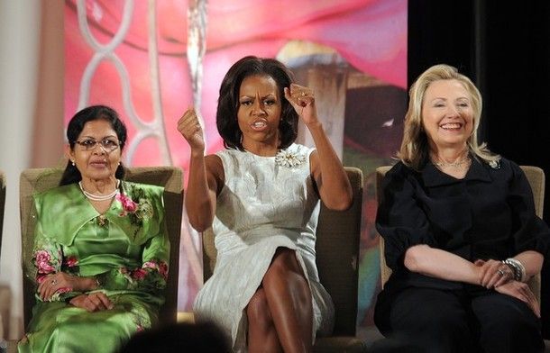 First Lady Michelle Obama, seated between Secretary of State Hillary Clinton and award recipient Aneesa Ahmed of Maldives at the 2012 International Women of Courage Awards ceremony at the State Department, leads the crowd in a cheer of 'Happy Women's Day!'