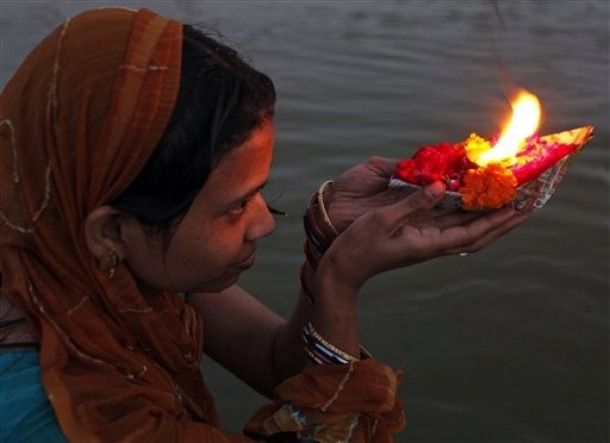 image of an Indian woman cradling a flame in her hands at the edge of a river