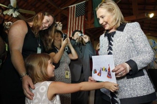 image of a little girl handing a drawing to Hillary Clinton, who smiles at her