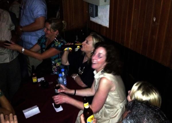image of Hillary Clinton sitting in a club, drinking a beer, flanked by laughing women