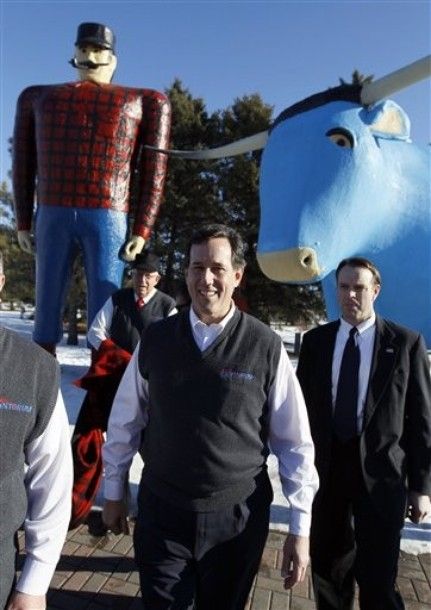 Rick Santorum walking away from a photo-op near giant statues of Paul Bunyan and Babe the Blue Ox