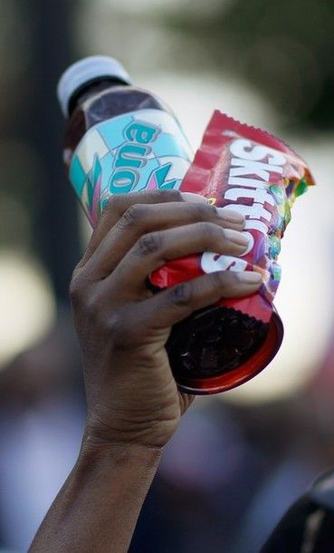 image of the hand of a young black person holding up a bottle of iced tea and a bag of Skittles