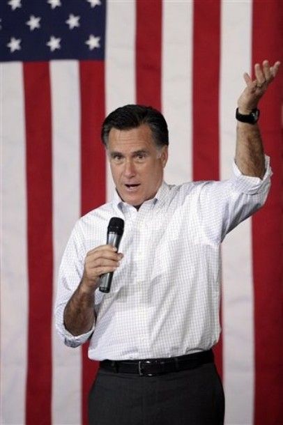 Romney stands in front of a flag, speaking into a mic, and throwing up his hand