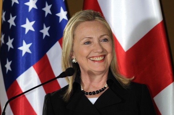 image of Hillary Clinton, standing in front of a US flag, smiling