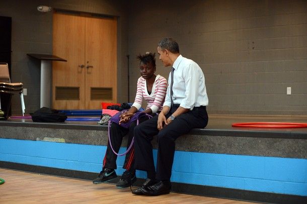 President Obama sitting on the edge of a stage with an African-American young woman