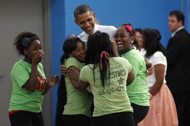 image of President Obama being hugged by three very excited African-American young women, while a fourth stands beside them, covering her mouth in excitement