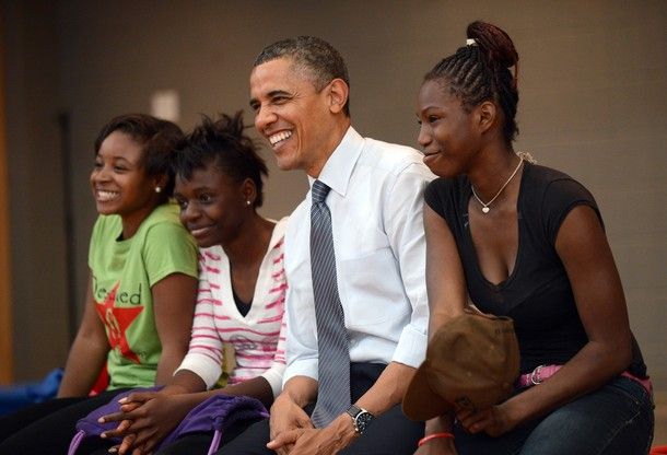 image of President Obama sitting on the edge of a stage with three African-American young women