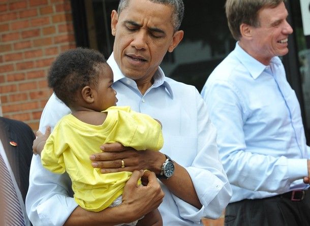 image of President Barack Obama at a campaign event, holding a black baby boy in a yellow t-shirt