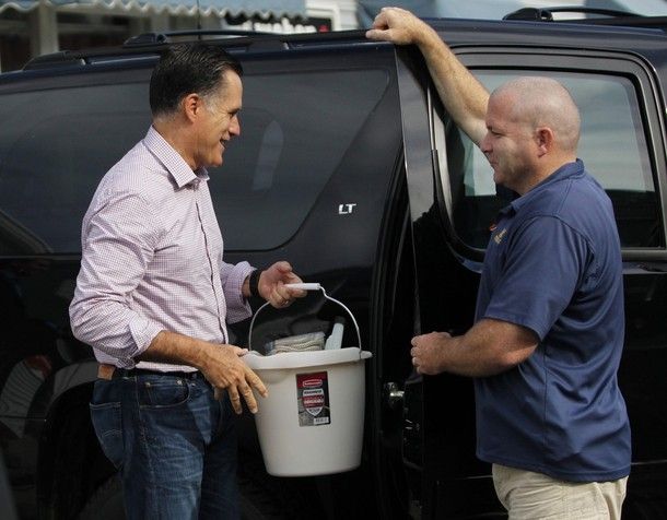 image of Mitt Romney holding a bucket full of junk, standing beside a black vehicle talking to a middle-aged white man