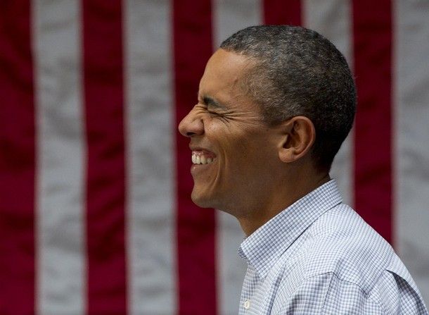 image of President Barack Obama standing in profile in front of a US flag, his face scrunched up with laughter