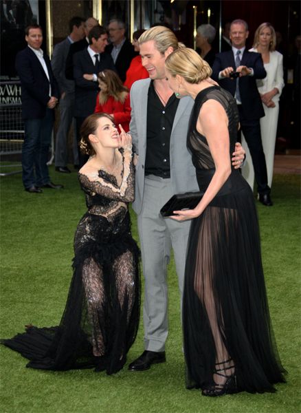 Kristen Stewart, in a black lace dress, makes a face and flips the birth as she crouches next to Chris Hemsworth, in a grey suit, and Charlize Theron, in a black gown