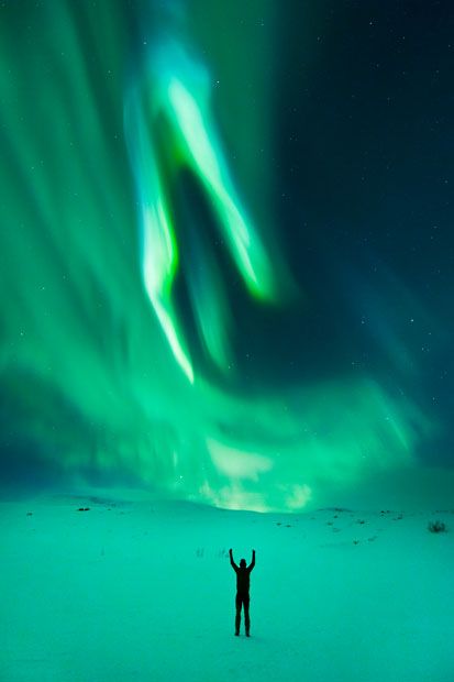 image of a man in silhouette, in front of a beautiful and dramatic display of swooping, green Northern Lights