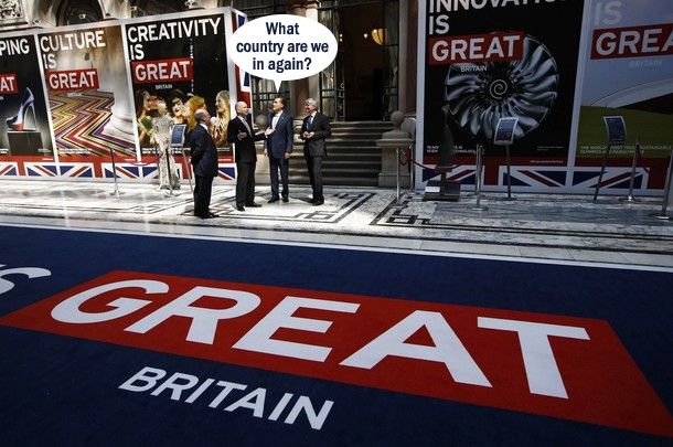 image of Mitt Romney visiting the UK, standing in the middle of a display with giant text reading 'GREAT BRITAIN' on the ground, to which I have added a dialogue bubble reading: 'What country are we in again?'