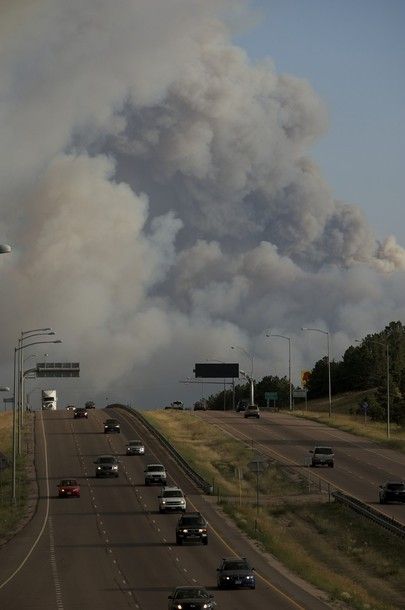 a plume of smoke rises high into the sky over a freeway