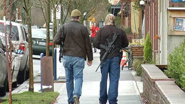 image of two white men strolling down the sidewalk with assault rifles