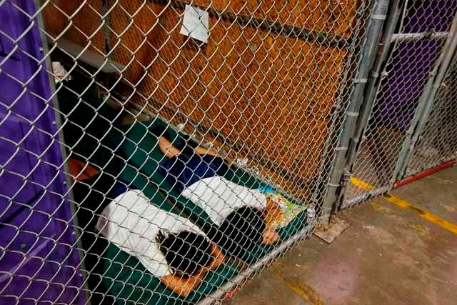 image of two small Latino children asleep in a tiny room behind a chain-link fence