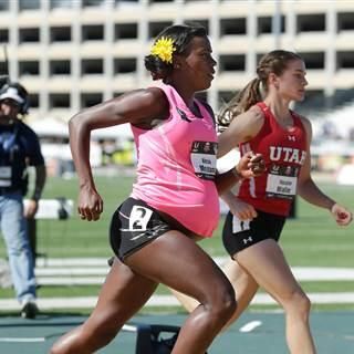 image of Montano running: She is a black, visibly pregnant woman wearing a yellow flower in her hair, a pink top, and black shorts