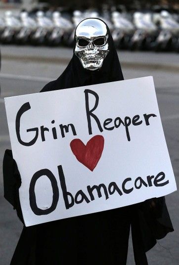image of a protestor in a black hooded robe and silver skull mask holding a handwritten sign reading: 'Grim Reaper [hearts] Obamacare'