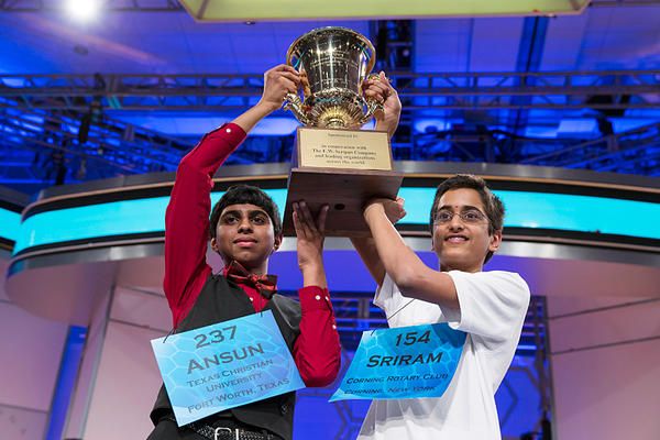 two young Indian-American boys together hold a trophy over their heads, smiling