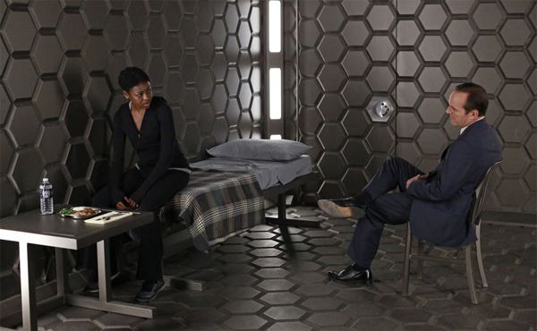 Agent Coulson (Clark Gregg, a middle-aged white man) sits in a honeycomb-walled jail cell talking to the prisoner, Akela Amador (Pascale Armand, a young black woman)