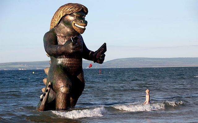 image of a 25-foot-high statue of a Godzilla-like creature with a face and hair like billionaire entrepreneur Richard Branson in the waves near the shore at an English beach