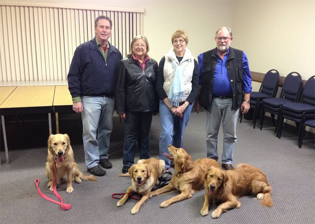 image of four middle-aged people who appear to be white with four golden retrievers