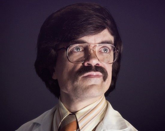 image of actor Peter Dinklage in an 80s wig, wire-framed glasses, and lab coat, and sporting a beautiful pornstache